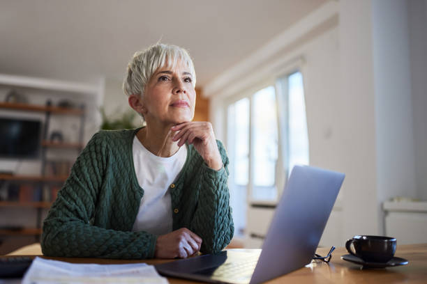 Mature woman thinking of something while working on a computer at home.